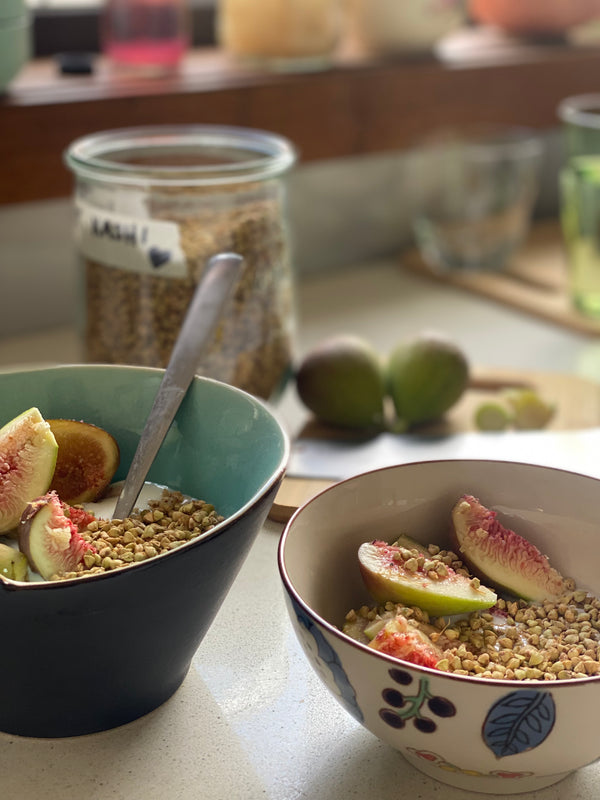 Two bowls of viili and figs and sprouted buckwheat kasha with the jar of it in the background along with some fresh figs on a chopping board. 