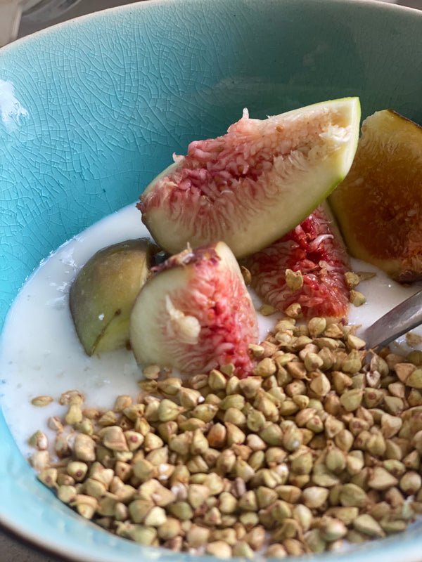 sliced fresh figs sitting atop and sinking into viili that looks like yoghurt, but shinier. There is a silver spoon hiding beneath some crunchy looking sprouted buckwheat. 